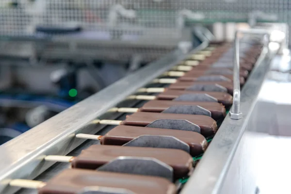 Linear Motion Food Processing Solutions Chocolate-coated ice cream bars moving along a stainless steel conveyor line in a hygienic food processing facility