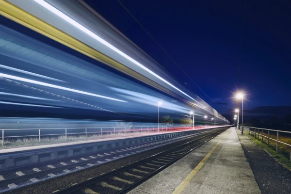High-speed passenger train passing through a station at night illustrating modern rail transport reliability